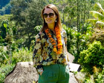 A woman with a lei smiles in a PNG village setting