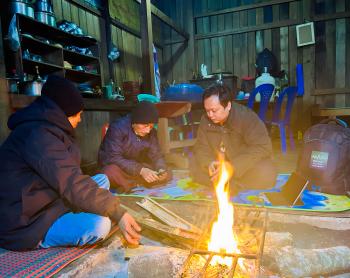 Men huddle around a smartphone by a fire in a hut