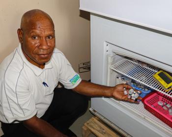 Karl Bafi displays vaccine vials next to the solar-powered vaccine refrigerator at Chuave Rural Hospital.