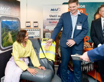 A woman sits on an aircraft seat whilst a man beckons another to sit