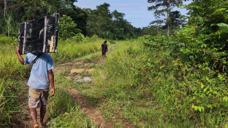 A Male carrying a solar panel while working on a muddy road heading into the remote community of Wasengla