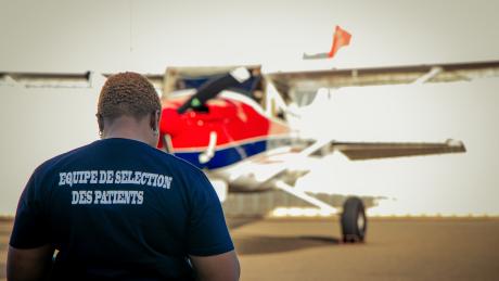 Mercy Ships patient selection staff member stands in front of MAF plane