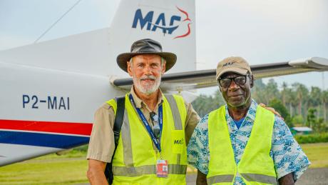 Two men stand in front of a plane