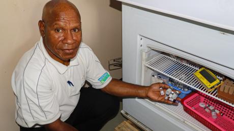 Karl Bafi displays vaccine vials next to the solar-powered vaccine refrigerator at Chuave Rural Hospital.