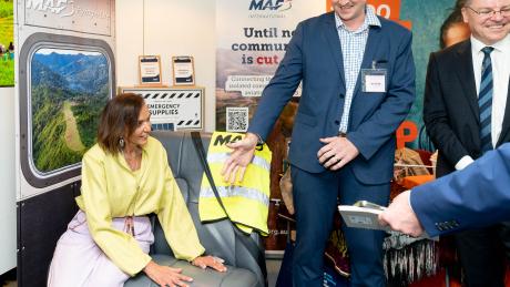 A woman sits on an aircraft seat whilst a man beckons another to sit