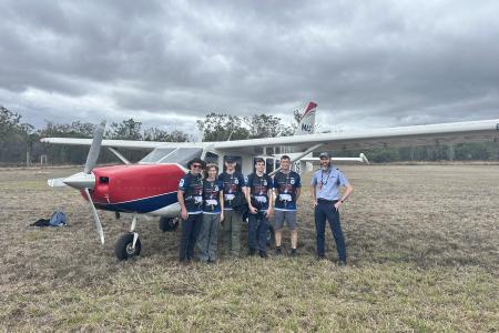Pilot and passengers standing in front of plane on grass airstrip