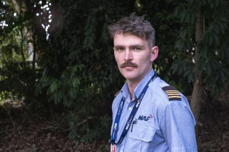 A pilot standing in the shade of a tree looking into camera