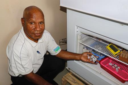 Karl Bafi displays vaccine vials next to the solar-powered vaccine refrigerator at Chuave Rural Hospital.