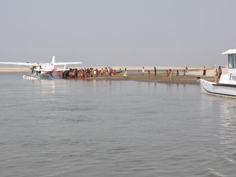 A floatplane rests on the water at anchor whilst local people look on