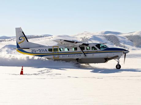 A plane lands on an airstrip with a light dusting of snow