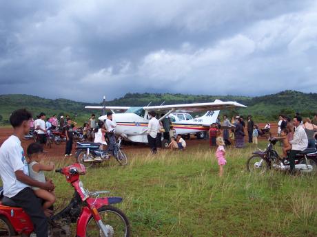 A small aeroplane parked on an airstrip is surrounded by onlookers