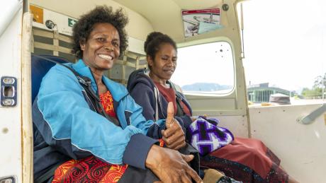 Nancy Berhard and another women sitting at the back seat of the MAF airplane on their way back to Wewak after the Pastor Women's course. Nancy gives a thumbs up.