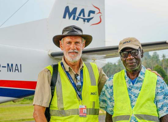 Two men stand in front of a plane