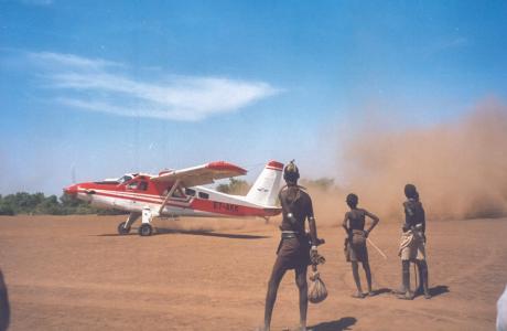 An aeroplane taxis on a dusty Ethiopian airstrip with local onlookers
