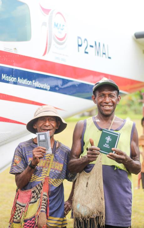 two locals from Munbil with bright smiles are posing with their newly purchased Tok Pisin Buk Baibels in front of the aircraft