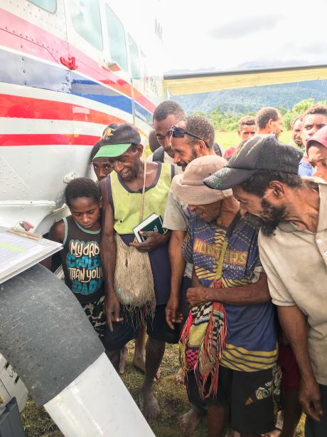 people crowded under the wing of the aircraft and looking down to the ground as this is where the pilot opened the Bible Box