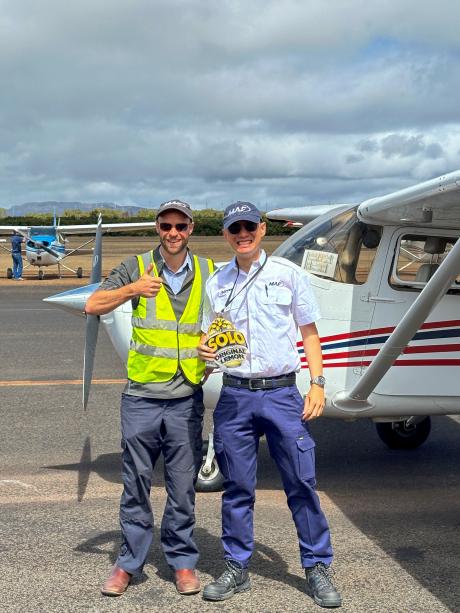 A student pilot poses with instructor by a small plane