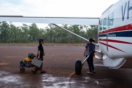 Woman wheeling small buggy to aircraft in rain