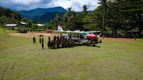erial view of MAF Cessna 208 P2-MAG at Yambaitok airstrip with locals gathered around.