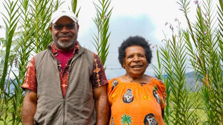 An adult son and his elderly mother stand and smile together