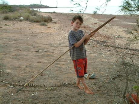 A young boy with a fishing spear on a beach