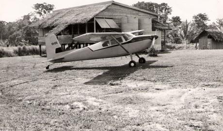 A plane on a remote airstrip with a house behind it