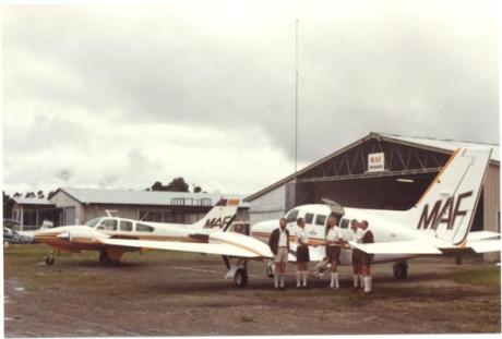 A group of people with two twin engine aeroplanes in front of a hangar