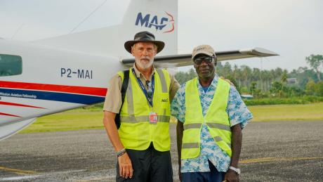 Two men stand in front of a plane